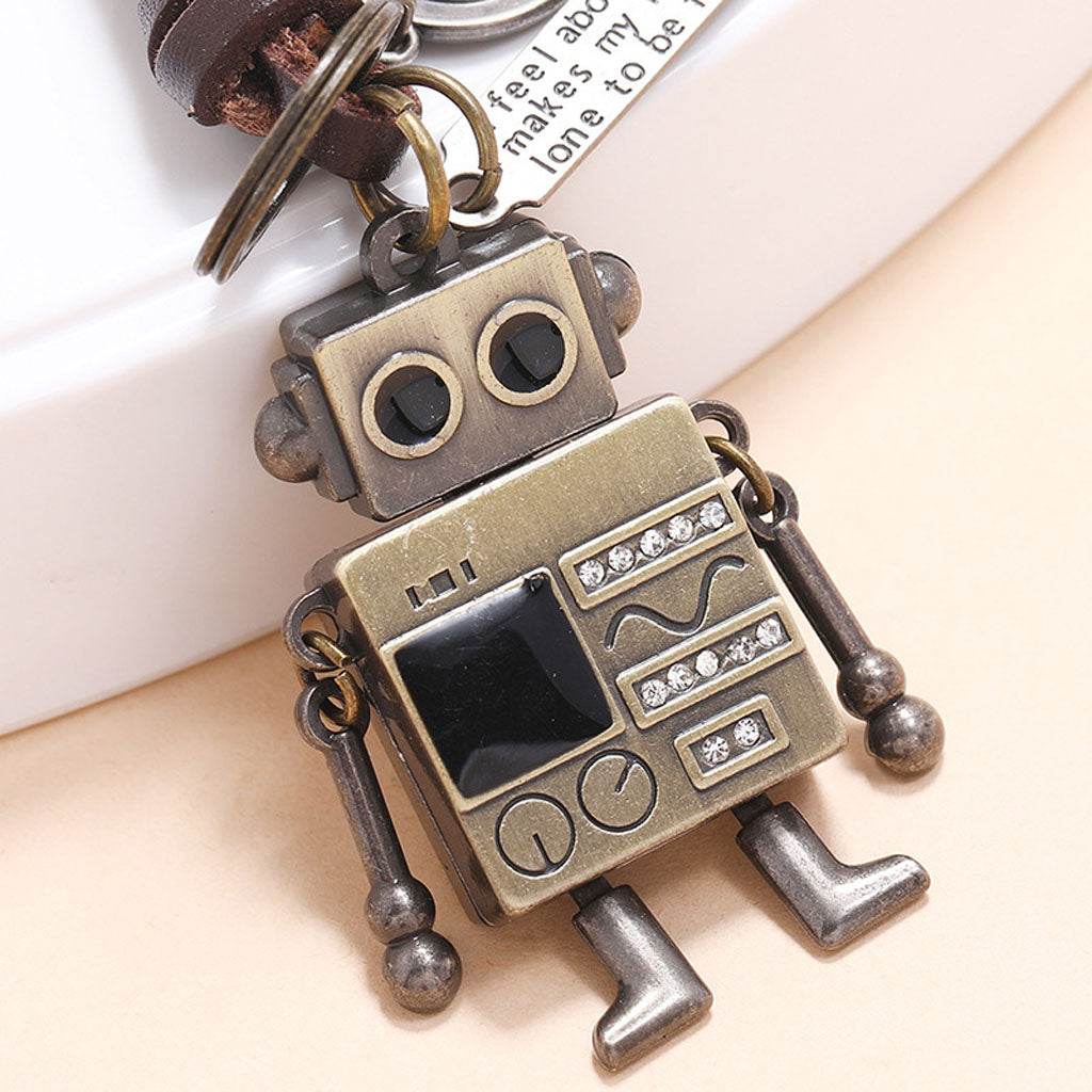 Close-up of a retro robot keychain, showing its movable arms, braided leather cord, and inspirational engraved tags.