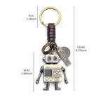 Close-up of a retro robot keychain, showing its movable arms, braided leather cord, and inspirational engraved tags.